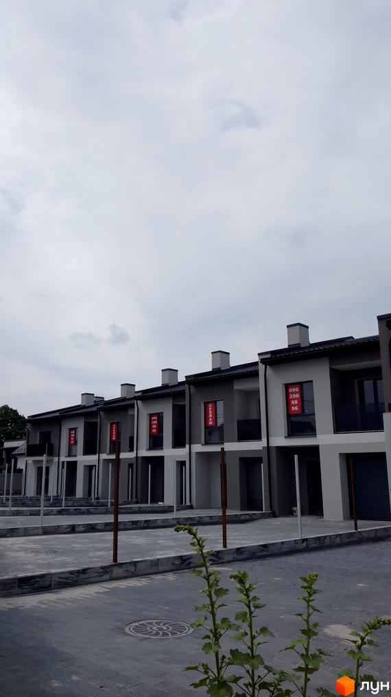 Ряд двоповерхових будинків сірих відтінків з темними дахами, що продаються на вул. Хмельницького, 6а. Прибудинкова територія вимощена плиткою.