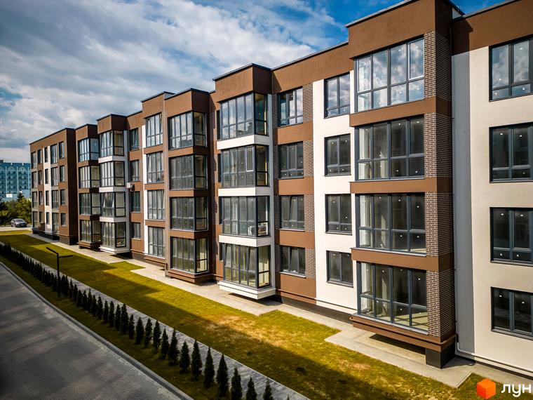 Житловий комплекс Royal Hill – це багатоповерхова новобудова з великими вікнами та коричнево-білим фасадом. Поруч розташований доглянутий газон та доріжка з туями.