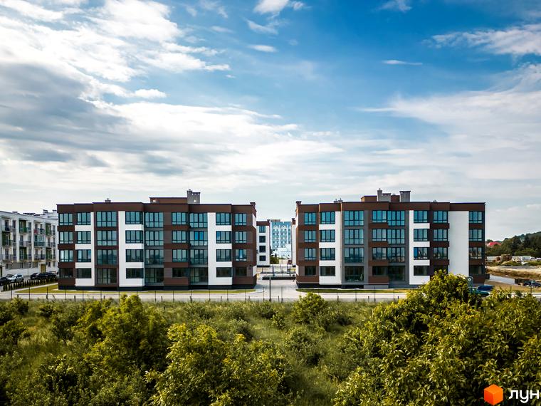 Житловий комплекс Royal Hill – це сучасна новобудова з коричнево-білим фасадом та великими вікнами. Територія навколо комплексу зелена та доглянута.