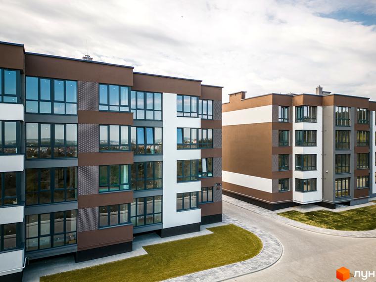 Зовнішній вигляд новобудови ЖК Royal Hill з коричнево-білими фасадами та великими вікнами. Прибудинкова територія з доглянутими газонами та доріжками.