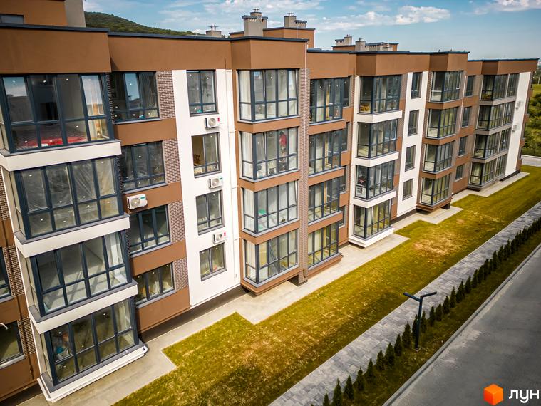 Зовнішній вигляд новобудови ЖК Royal Hill з коричневими та білими фасадами, великими вікнами та балконами. Поруч доглянута зелена територія з бруківкою та освітленням.