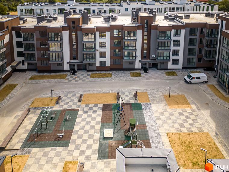 Вид на житловий комплекс Royal Hill з фасадами темно-коричневого та білого кольорів, прибудинкова територія з дитячим майданчиком та місцями для відпочинку.