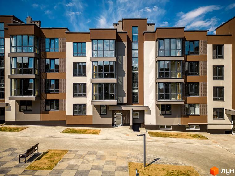 Фасад житлового комплексу Royal Hill з коричневими та бежевими елементами, великими вікнами та прибудинковою територією з лавкою та ліхтарем.