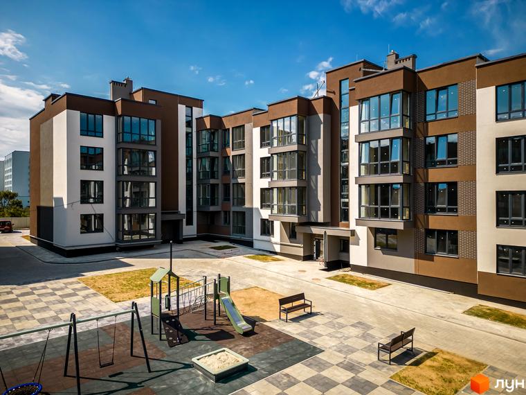 Зовнішній вигляд новобудови ЖК Royal Hill з коричневими та білими фасадами, великими вікнами та дитячим майданчиком з гойдалками та пісочницею.