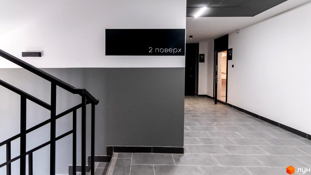 Інтер'єр сходової клітки в житловому комплексі Royal Hill з дверима та номерами квартир. Оздоблення стін білим та сірим кольором, чорні перила та чорна вивіска з написом 