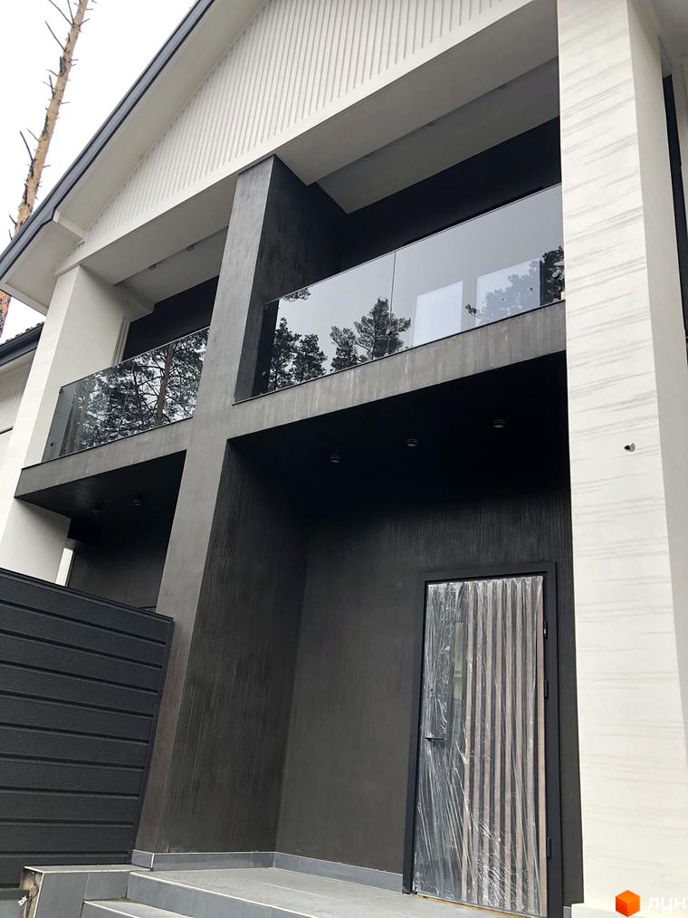 Сучасний фасад будинку Toscana Home з скляним балконом та темними елементами. Поруч розташована прибудинкова територія з парканом.