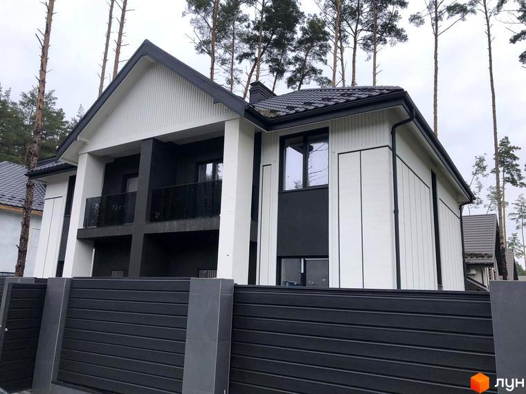 Сучасний дуплекс Toscana Home з біло-сірим фасадом та чорним парканом. Навколо будинку ростуть високі дерева.