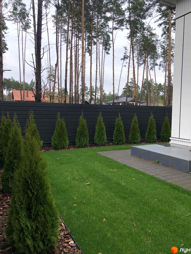 Зображення фасаду будинку в Toscana Home. Зелена трава, туї та паркан створюють затишну атмосферу.