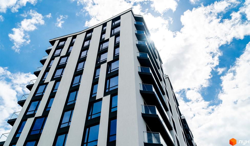 Сучасний житловий комплекс Авторський з панорамними вікнами та скляними балконами на фоні блакитного неба з хмарами. Зовнішній вигляд будівлі з білими та чорними елементами фасаду.