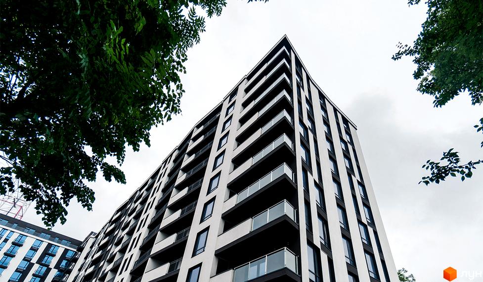 Новобудова ЖК Авторський з біло-чорним фасадом та скляними балконами, оточена зеленню дерев.