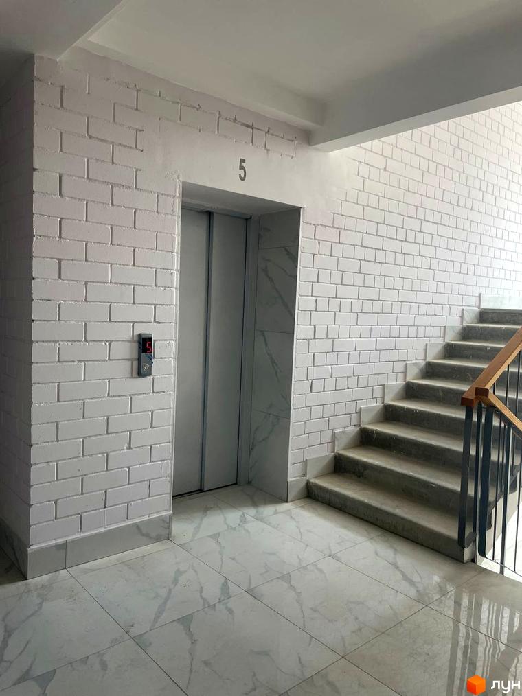 Житловий комплекс на Масанах: внутрішній простір з білими цегляними стінами та мармуровою плиткою біля ліфта та сходів.