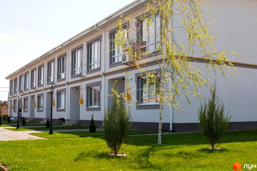 Зображення фасаду будинку в Котеджному містечку Паларіс. На передньому плані доглянутий газон та дерева.