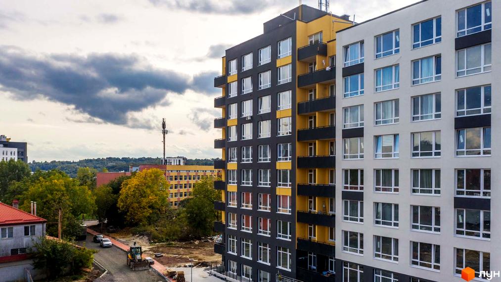 Житловий комплекс Білий Шоколад - фасади будівель з жовтими та сірими елементами, вікнами та балконами. На прибудинковій території дорога, дерева та будівельна техніка.