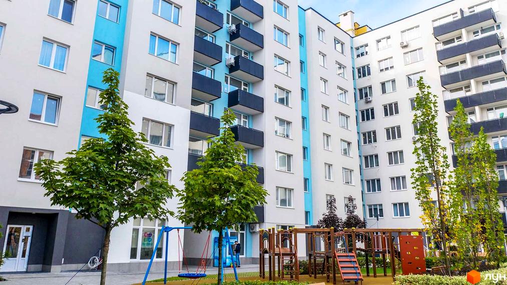 Житловий комплекс Білий Шоколад з біло-блакитним фасадом та балконами, дитячим майданчиком та деревами на прибудинковій території.