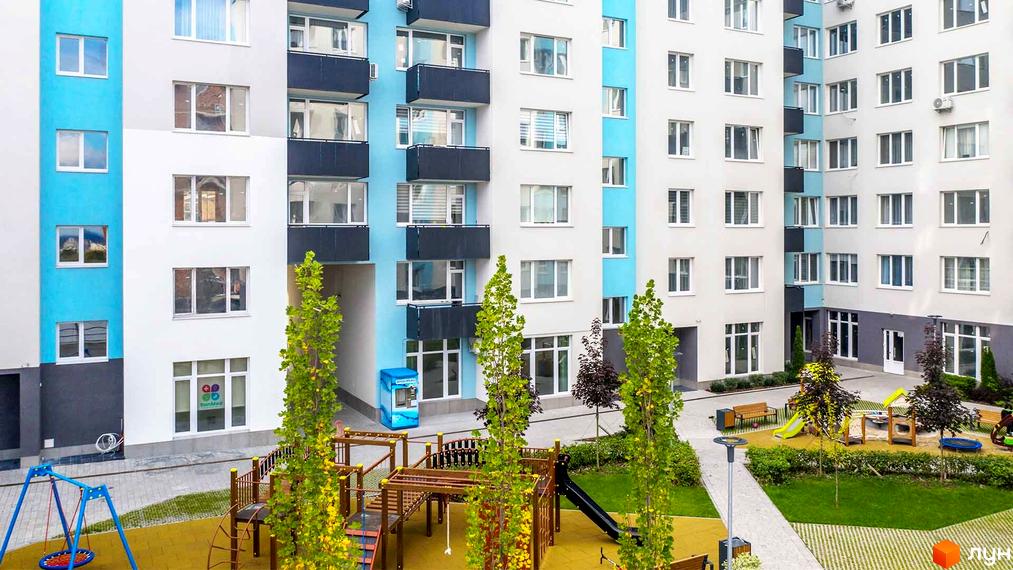 Житловий комплекс Білий Шоколад з фасадом у біло-блакитних тонах та дитячим майданчиком на прибудинковій території.