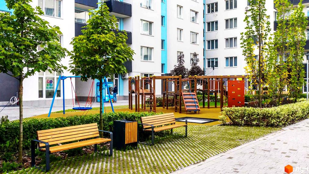 Житловий комплекс Білий Шоколад: сучасний фасад будинку та обладнаний дитячий майданчик з гойдалками та лавками.