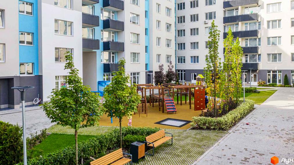 Житловий комплекс Білий Шоколад: фасади будівель з блакитними та білими елементами, дитячий майданчик з гірками та лавочки на прибудинковій території.