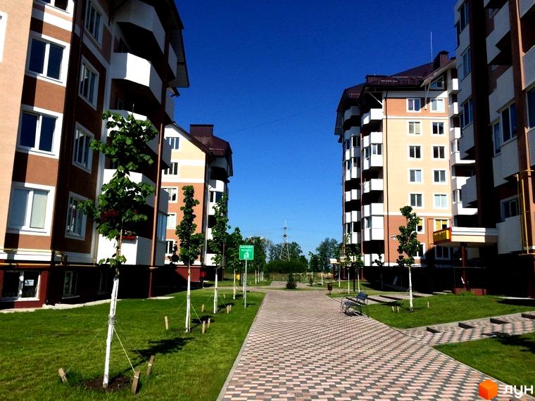 Зовнішній вигляд житлового комплексу Квартал Буча з сучасними фасадами. Прибудинкова територія з зеленими насадженнями та пішохідними доріжками.