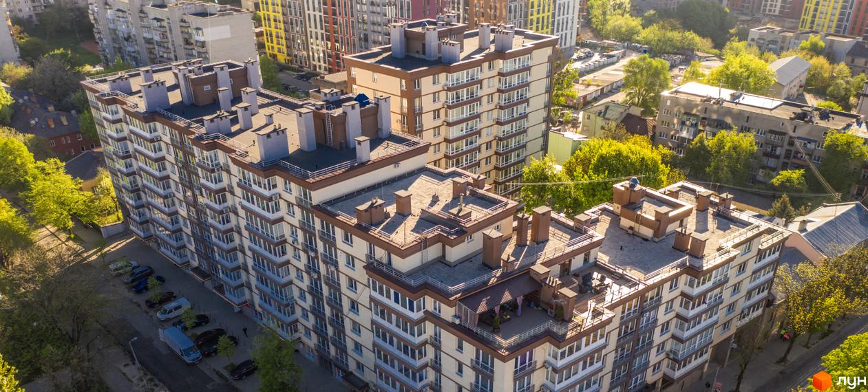 Житловий комплекс Шоколад: багатоповерхові будинки зі світлими фасадами, коричневими балконами та дахами. Навколо зелені дерева та прибудинкова територія з автомобілями.