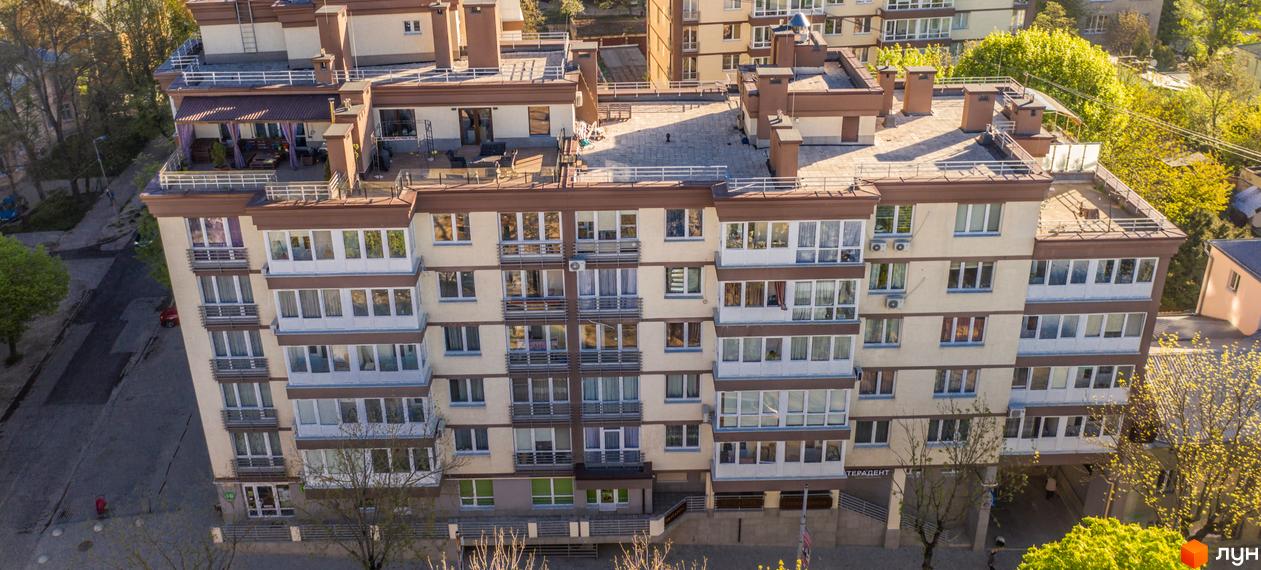 Багатоповерховий Житловий комплекс Шоколад з бежевими стінами, коричневими акцентами, балконами та терасою на даху. Поруч дорога та дерева.