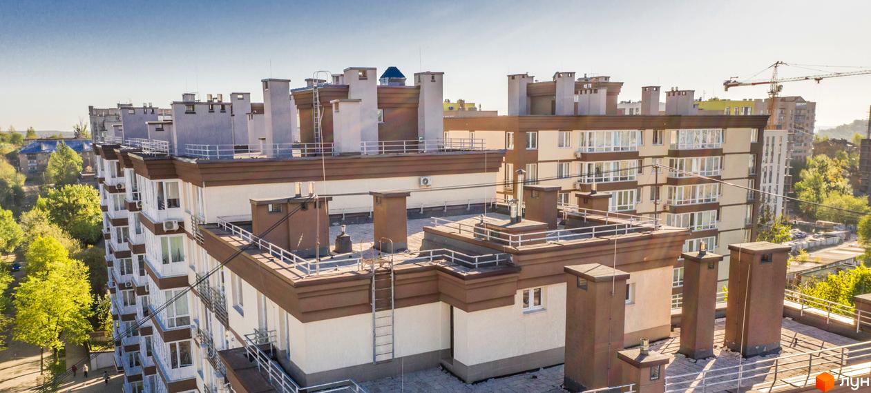 Житловий комплекс Шоколад – багатоповерхова будівля зі світлими стінами, коричневими елементами та балконами. На даху видно технічні споруди, а навколо – зелені дерева.