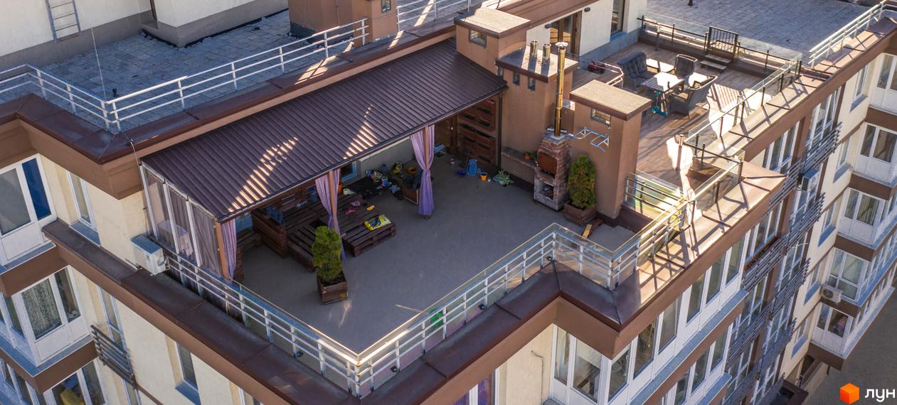 Житловий комплекс Шоколад: багатоповерховий будинок з бежевими фасадами та коричневими елементами. На даху облаштована тераса з зоною відпочинку, альтанкою та барбекю.