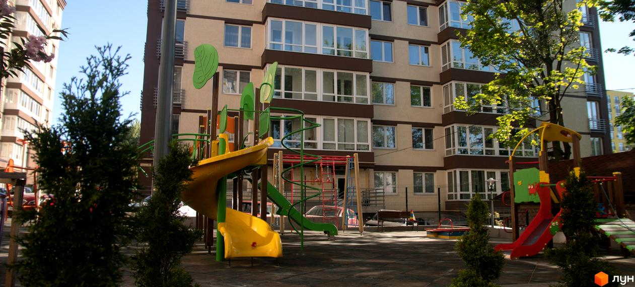 Багатоповерховий будинок Житлового комплексу Шоколад з бежевими фасадами та коричневими акцентами, поруч дитячий майданчик з гірками.