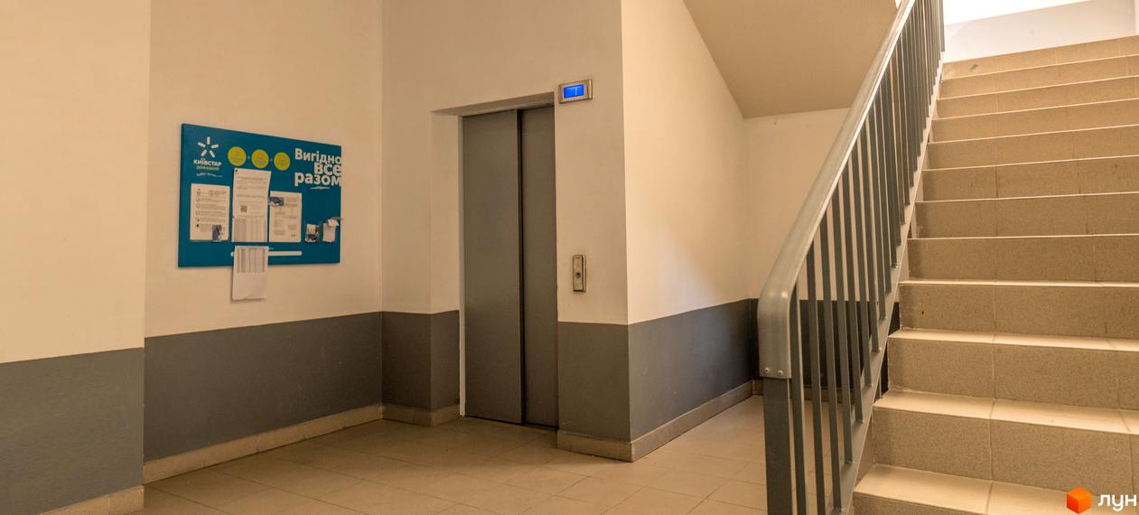 Внутрішній простір Житлового комплексу Шоколад: хол з двоколірними стінами, ліфт, сходи з металевими поручнями та інформаційний стенд.