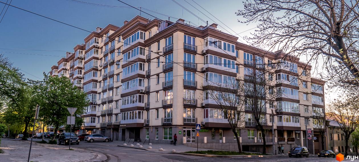 Багатоповерховий житловий комплекс Шоколад з бежевим фасадом та коричневими балконами. Розташований біля дороги з припаркованими автомобілями та зеленими деревами.