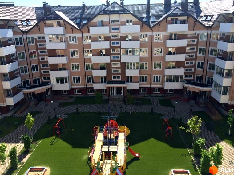 Житловий комплекс Квартал Буча з фасадами світло-бежевого кольору, білими балконами та зеленим внутрішнім двором з дитячим майданчиком. Вид зверху на будівлю та прибудинкову територію.