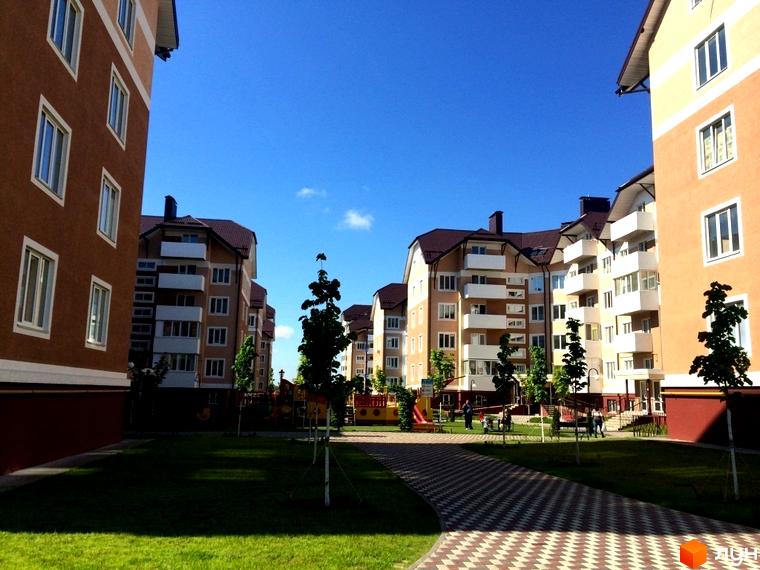 Житловий комплекс Квартал Буча. Багатоквартирні будинки з коричневими та бежевими фасадами, балконами та зеленим подвір'ям з дитячим майданчиком.