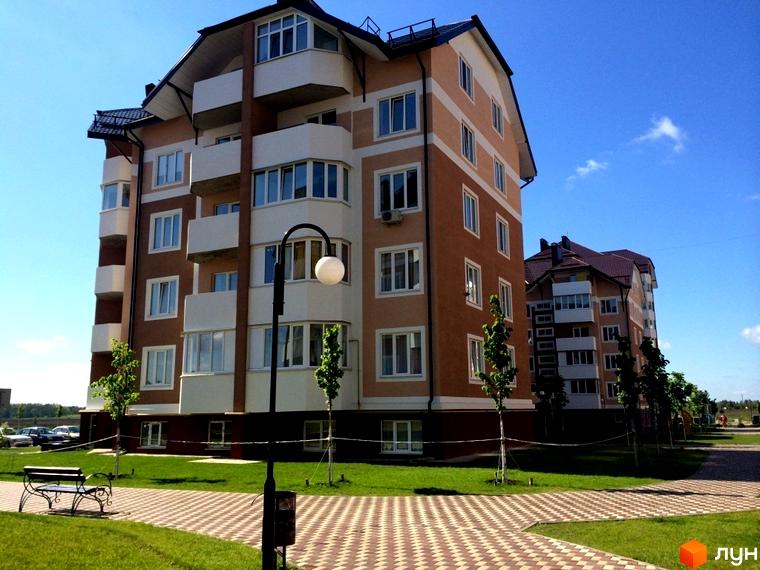 Житловий комплекс Квартал Буча. Зовнішній вигляд будинку з балконами та вікнами, прибудинкова територія з лавкою та деревами.