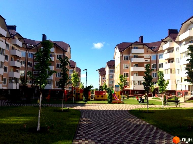 Житловий комплекс Квартал Буча. Багатоквартирні будинки з балконами та коричневими дахами, зелена прибудинкова територія з дитячим майданчиком.