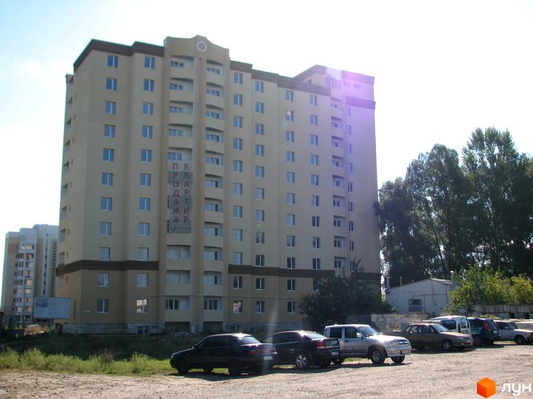 Житловий комплекс Уюткіно з багатоповерховим будинком та прибудинковою територією, де розташовані автомобілі.