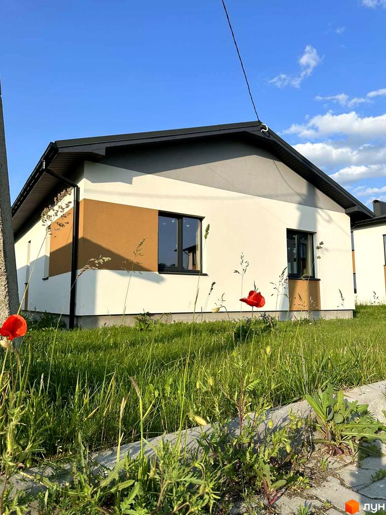 Зовнішній вигляд будинку в Котеджному містечку Горіхова Долина. Навколо будинку зелена трава та квіти.