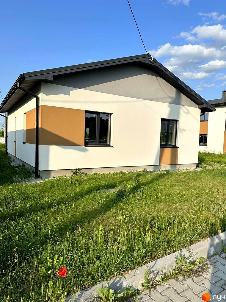 Зовнішній вигляд будинку в Котеджному містечку Горіхова Долина. Навколо будинку зелений газон та тротуарна плитка.