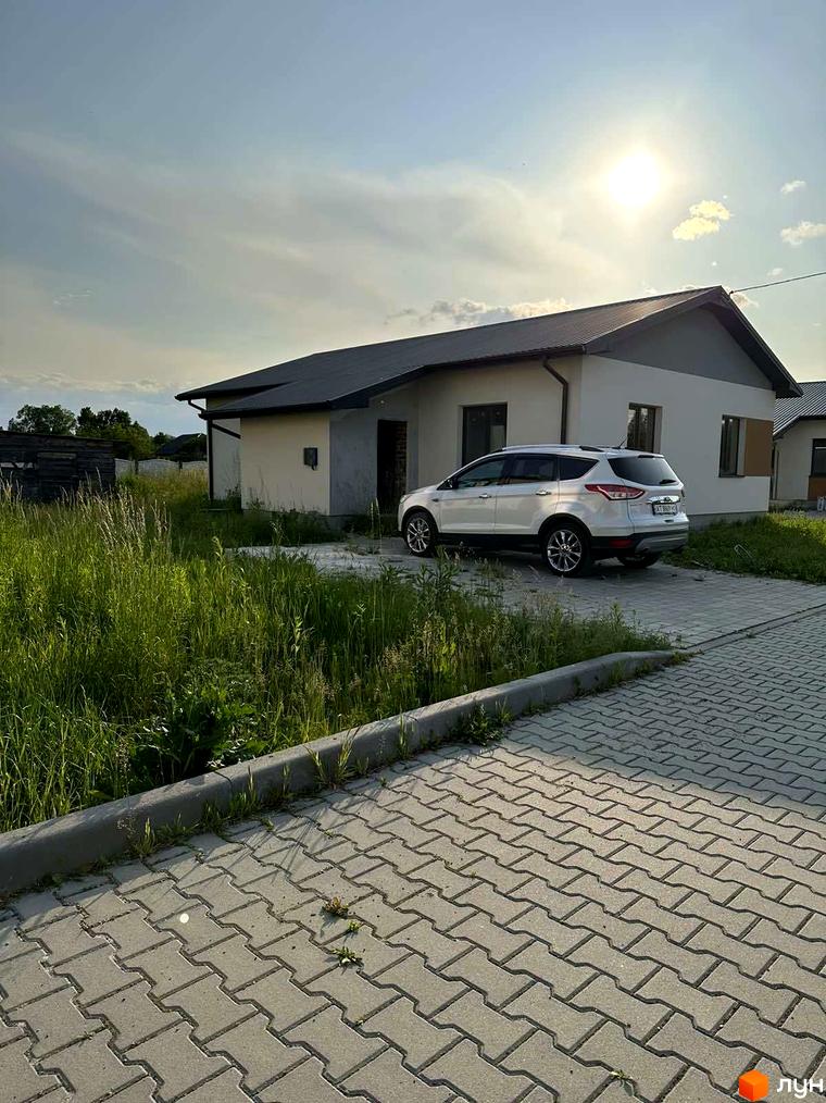 Фото будинку в Котеджному містечку Горіхова Долина. На передньому плані видно автомобіль та прибудинкову територію з тротуарною плиткою.