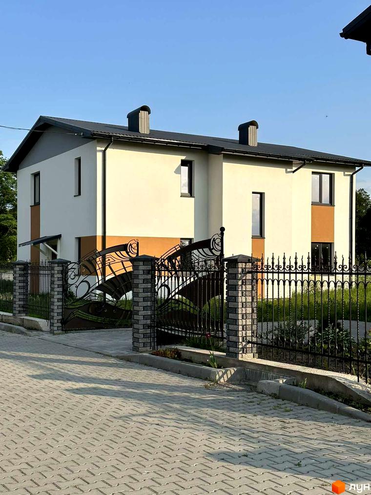 Двоповерховий будинок з білим фасадом та сірим дахом в Котеджному містечку Горіхова Долина. Перед будинком кована огорожа та тротуарна плитка.