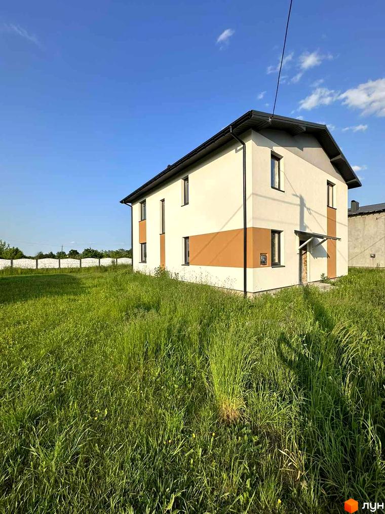 Зображення двоповерхового будинку з коричневими вставками в Котеджному містечку Горіхова Долина. Навколо будинку висока трава.
