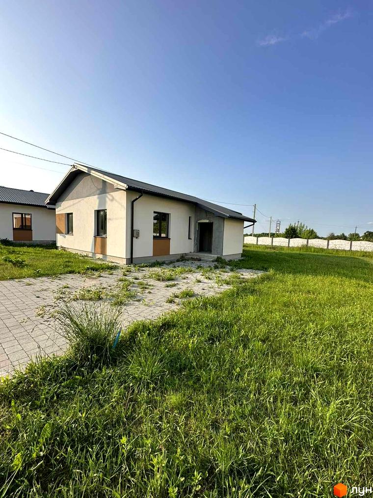 Фото Котеджного містечка Горіхова Долина. Одноповерховий будинок з сірою покрівлею та світлим фасадом на зеленій галявині.