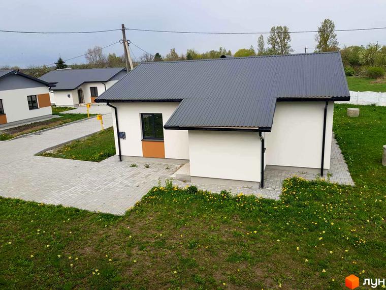 Вигляд котеджу в Котеджному містечку Горіхова Долина з сірим дахом та білими стінами. Навколо будинку зелений газон та тротуарна плитка.