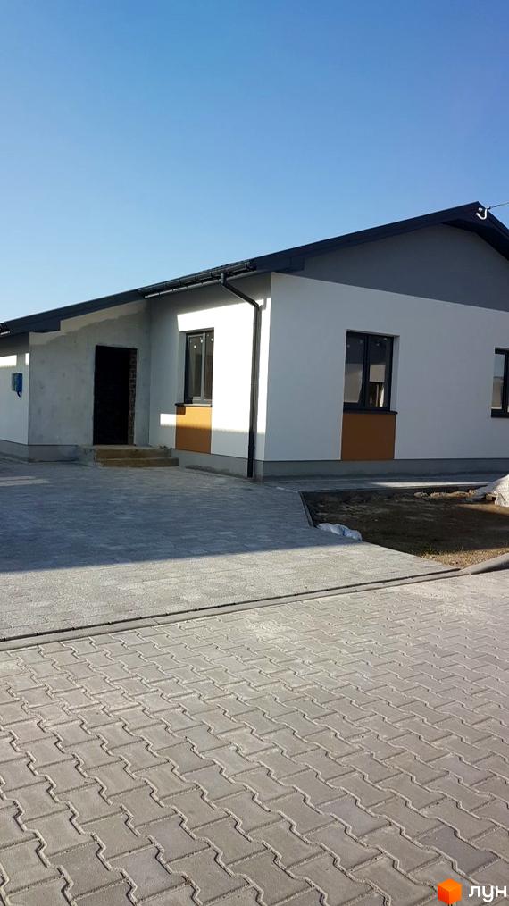 Зображення будинку в Котеджному містечку Горіхова Долина з сірою бруківкою перед ним. Фасад будинку білий з чорними вікнами.