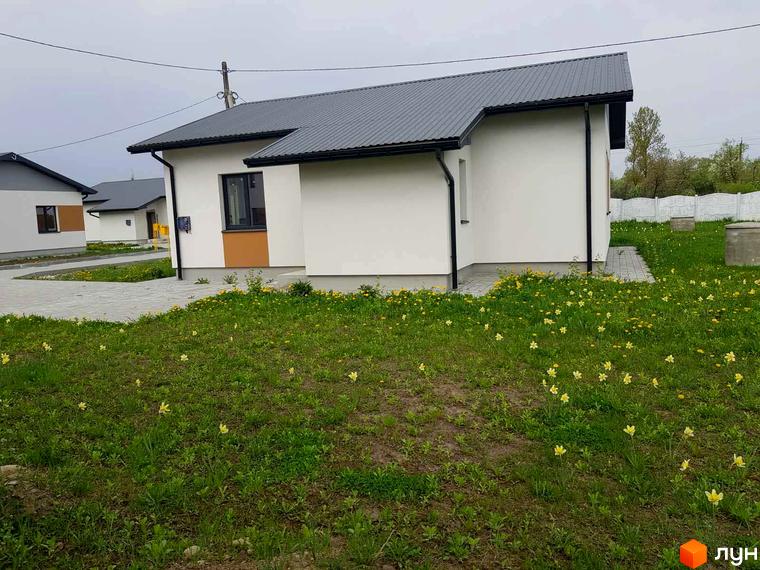 Зображення будинку в Котеджному містечку Горіхова Долина. Навколо будинку зелений газон з жовтими квітами.