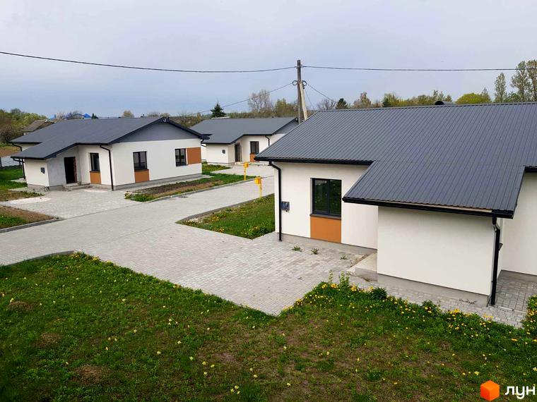 Фото Котеджного містечка Горіхова Долина: одноповерхові будинки з сірими дахами та білими стінами. Подвір'я з бруківкою та зеленим газоном.