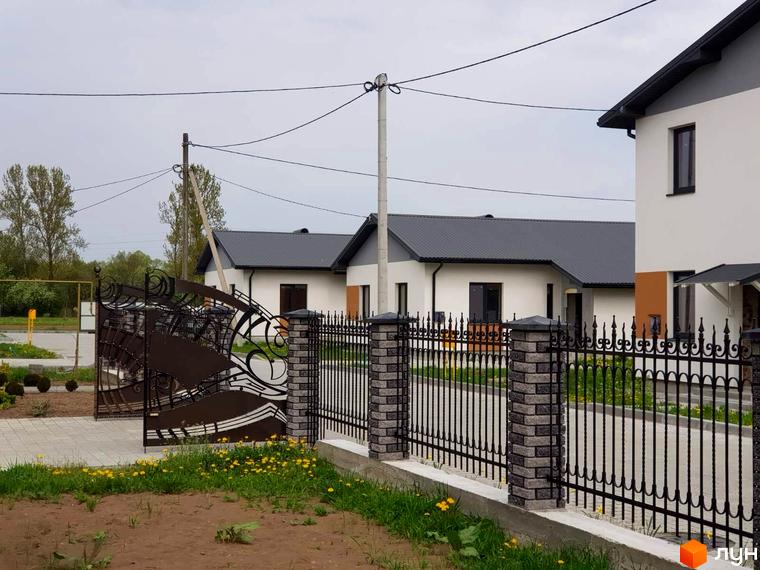 Фото Котеджного містечка Горіхова Долина: одноповерхові будинки з сірими дахами та білими стінами, огороджені кованою огорожею.