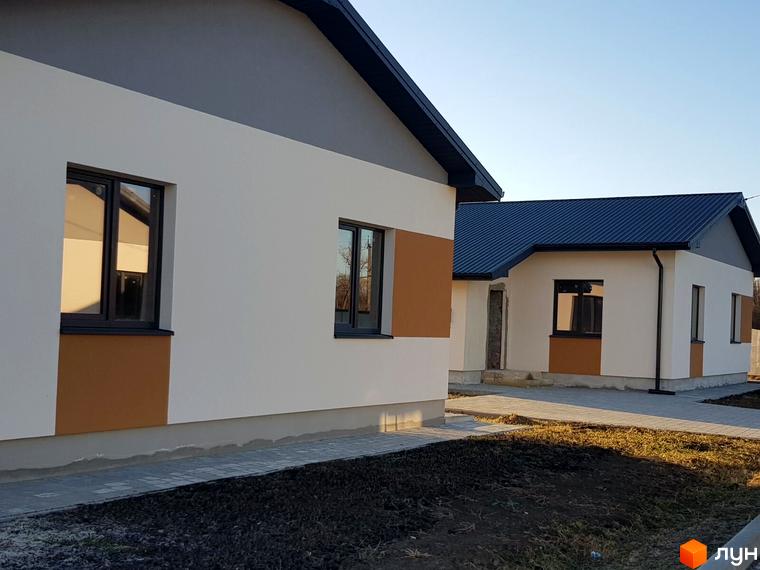 Зображення Котеджного містечка Горіхова Долина. Одноповерхові будинки з темними вікнами та дахом, білі стіни з коричневими вставками, доріжка з плитки.