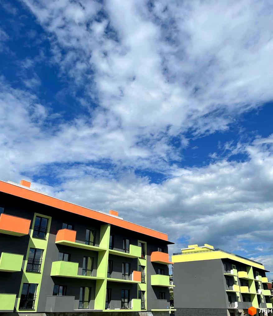 Зображення фасаду Житлового району Долина Троянд з балконами та яскравим оздобленням на фоні блакитного неба з хмарами.