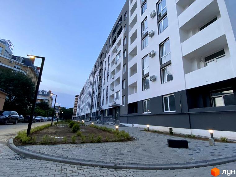 Житловий комплекс Щасливий: фасади будівель з кондиціонерами та балконами, вимощена алея та освітлення прибудинкової території.