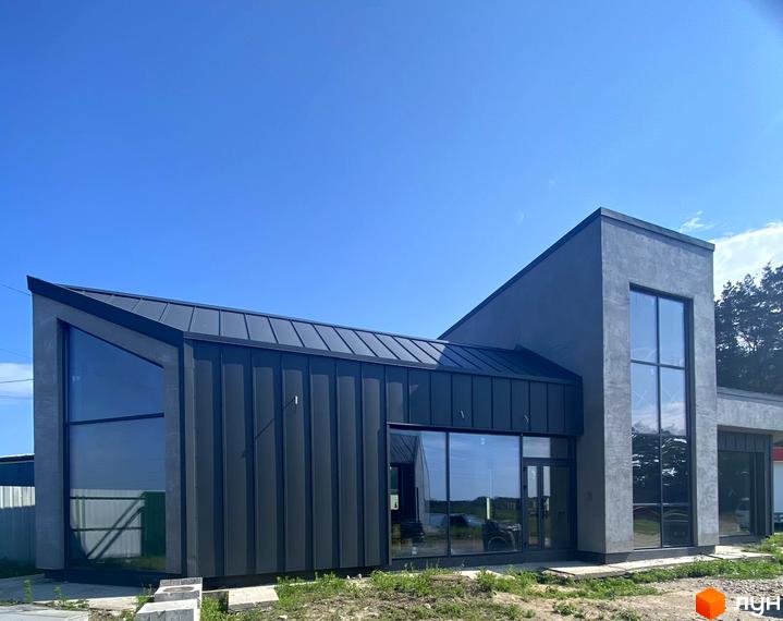 Зовнішній вигляд будинку КМ Нова Конча-Заспа CRYSTAL з великими вікнами та темним фасадом. Навколо будинку видно зелену територію та блакитне небо.