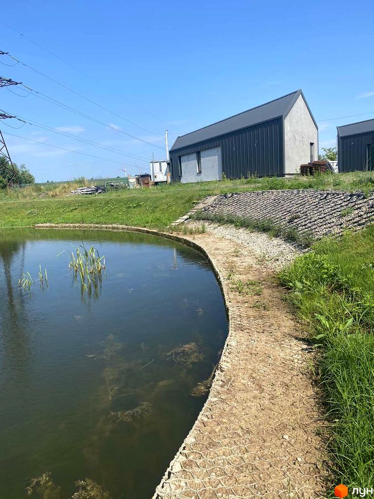 Котеджне містечко Нова Конча-Заспа CRYSTAL з сірими фасадами та темними дахами, розташоване біля водойми з зеленою прибудинковою територією.